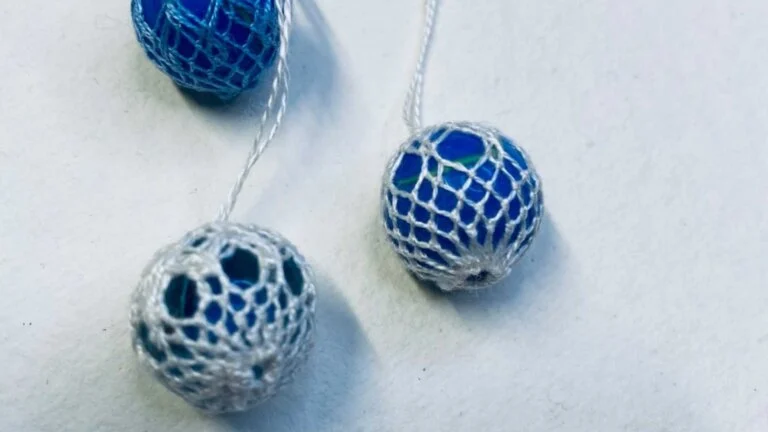 Blå perler i heklet netting, tre stykker, på hvit bakgrunn. Håndlagde dekorasjoner med delikat mønster.