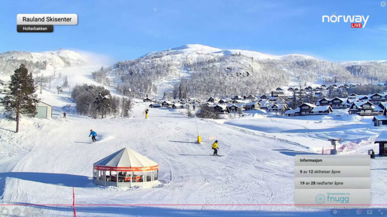 Skikjørere i Rauland Skisenter med snødekte fjell og hytter i bakgrunnen på en solfylt vinterdag.