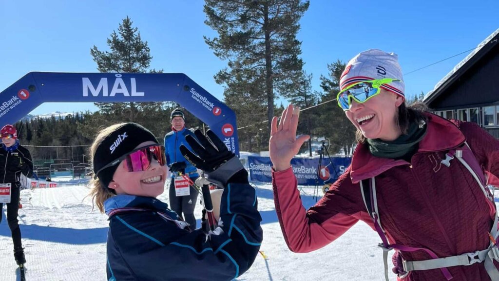 Twee skiërs geven elkaar een high-five bij de finishlijn in zonnig weer.