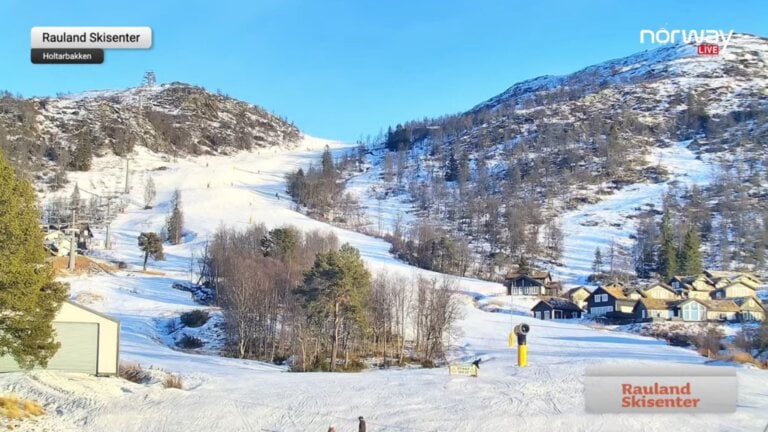 Skibakke på Rauland Skisenter i strålende vær med snødekte fjell, hytter og klare blå himmel.