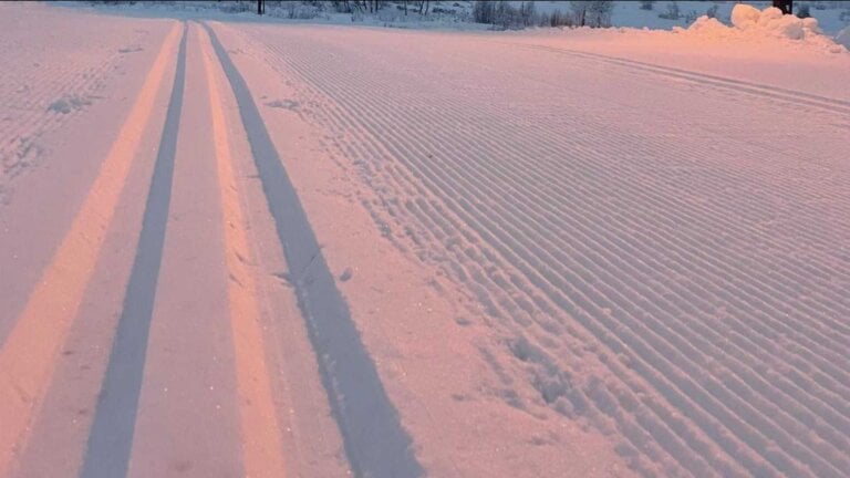 Langrennsspor ved solnedgang i snødekt landskap, perfekt preparert for ski.