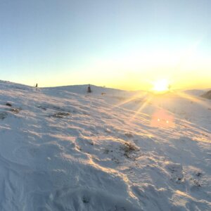 Vinterlandskap med snøkledde fjell i solnedgang, en stor skulptur og klar blå himmel.