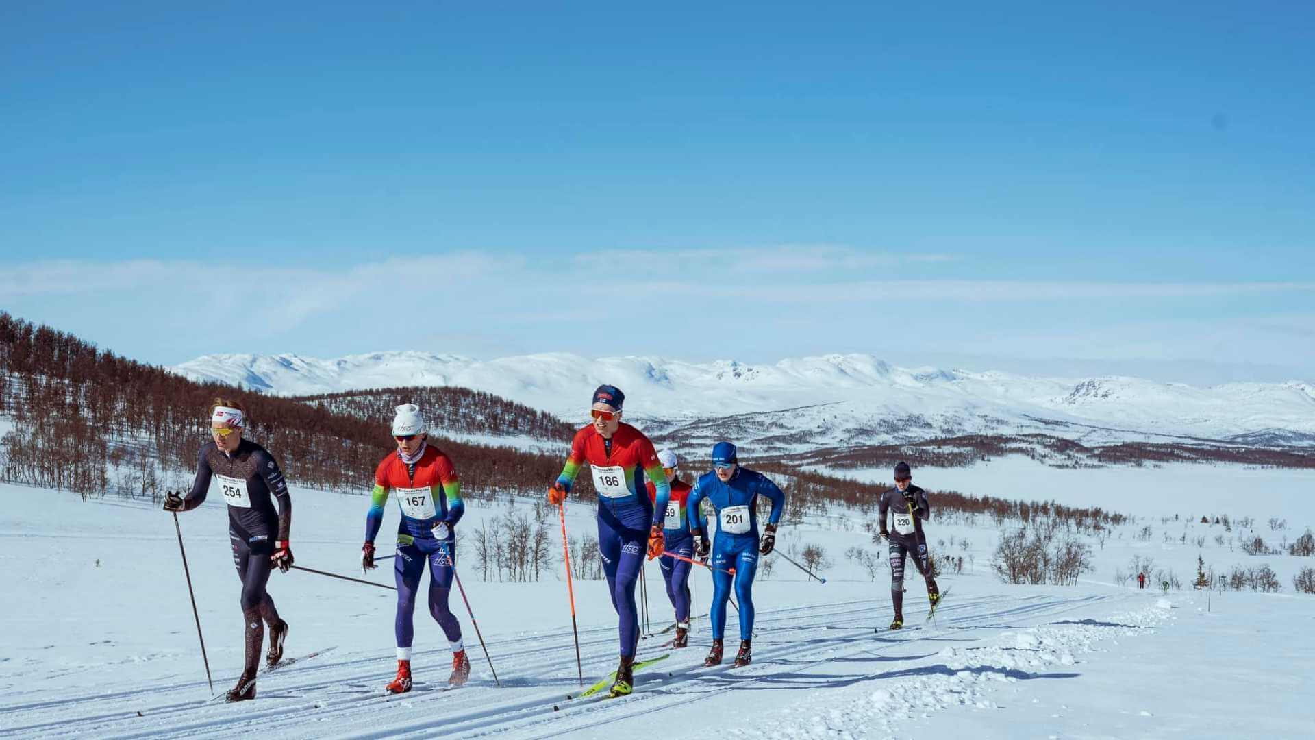 Langrennsløpere konkurrerer i vakkert snødekt landskap under en solfylt dag i fjellene.