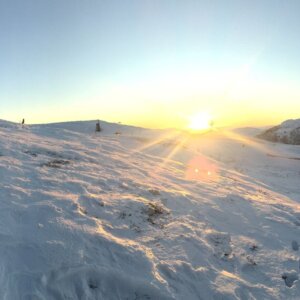 Soloppgang over snødekket fjellandskap med blå himmel. Perfekt for vinteraktiviteter og spektakulær natur.