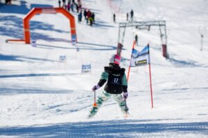 Barn i skikurs kjører ned slalåmbakke med nummer 17 på rygg, mot snødekt målområde og fargerike porter.