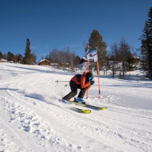 Person som står på ski i høy fart ned en snødekt bakke under klar blå himmel.