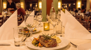 Steak serveres på en elegant restaurantbord med vin og levende lys.