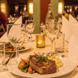 Steak serveres på en elegant restaurantbord med vin og levende lys.