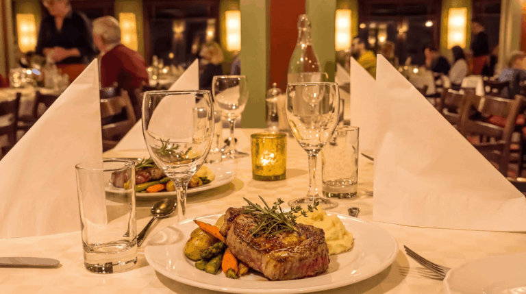 Steak serveres på en elegant restaurantbord med vin og levende lys.