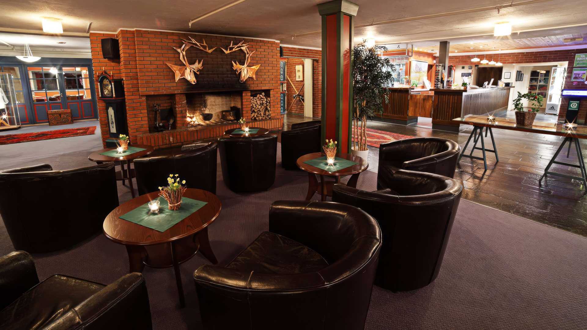 Koselig hotellobby med lenestoler og peis, mørke møbler og dempet belysning for en avslappende atmosfære.