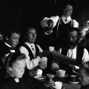 En gruppe mennesker i tradisjonelle klær, drikker te rundt et bord. Gammeldags atmosfære.