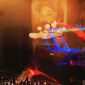 DJ spiller musikk i mørk klubb, fargerike lysstriper i bevegelse.