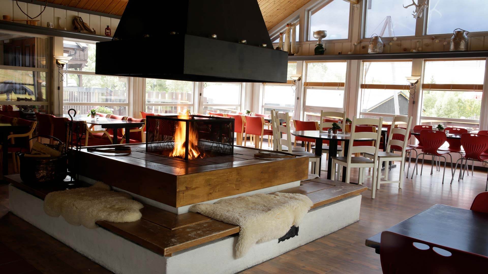 Koselig kaféinteriør med peis, myke stoler og store vinduer som slipper inn naturlig lys.