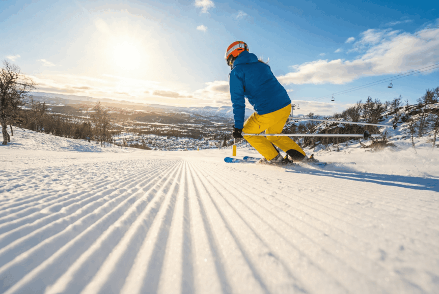 Person på ski ned solfylt fjellbakke i Norge, med frisk snø og blå himmel rundt.