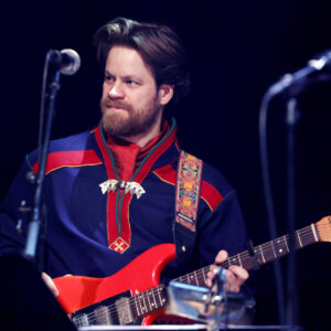 Musiker spiller elektrisk gitar i tradisjonell drakt på scenen.