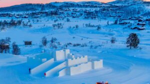 Snøslott i vinterlandskap med fjellhytter i bakgrunnen under solnedgang i Norge.