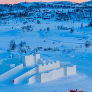 Snøslott i vinterlandskap med fjellhytter i bakgrunnen under solnedgang i Norge.