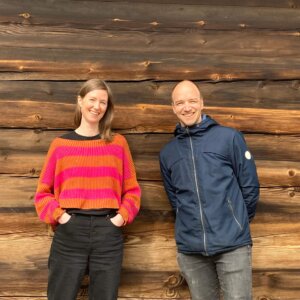 To mennesker smiler foran en vegg av treverk.