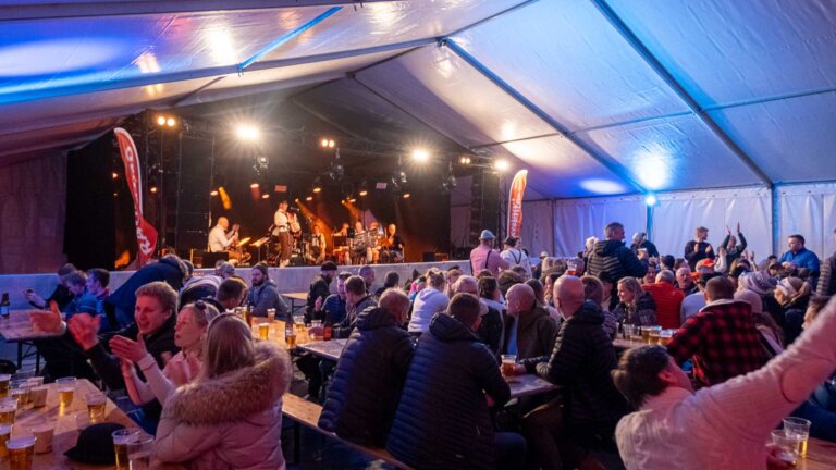 Folkemengde nyter konserten i et opplyst telt, mens bandet spiller på scenen under en festival.