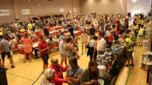 Folkemasse på loppemarked med boder, salg av varer og mennesker som interagerer i en innendørs hall.