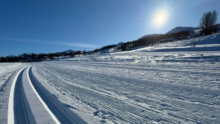 Fjellsjø med skiløyper og strålende solskinn på en klar vinterdag. Perfekt for langkjøring og utendørs aktiviteter.