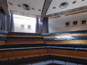 Amfiteatersal med trebenker og blå puter, takvinduer slipper inn lys, minimalistisk design, tomt auditorium.