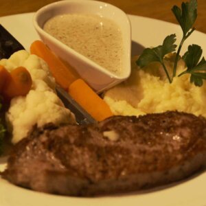 Biffmiddag med potetmos, grønnsaker og saus på tallerken, pyntet med persille.