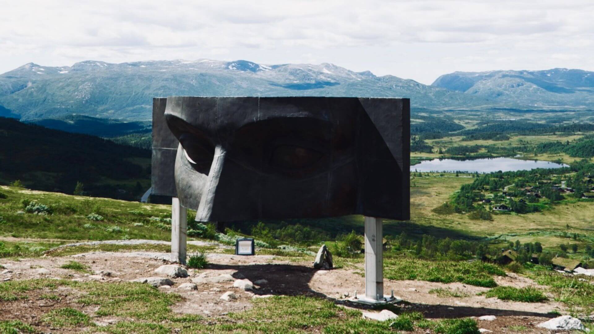 Sculptur av et ansikt med fjell og vann i bakgrunnen, som skaper en fantastisk naturscene i Norge.