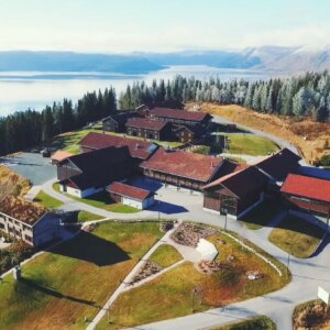 Alt-tekst: Luftbilde av en hyttekompleks med naturskjønn utsikt over innsjø og fjell i Norge.