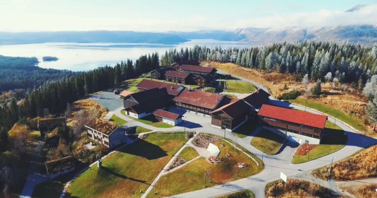 Alt-tekst: Luftbilde av en hyttekompleks med naturskjønn utsikt over innsjø og fjell i Norge.