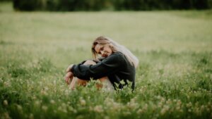 Ung kvinne sitter i en blomstereng, iført en mørk genser, med et tankefullt uttrykk.