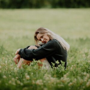 Ung kvinne sitter i en blomstereng, iført en mørk genser, med et tankefullt uttrykk.