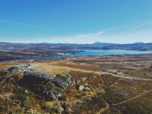 Utsikt over daler og innsjøer fra en høyde, med fjell i bakgrunnen på en klar høstdag.
