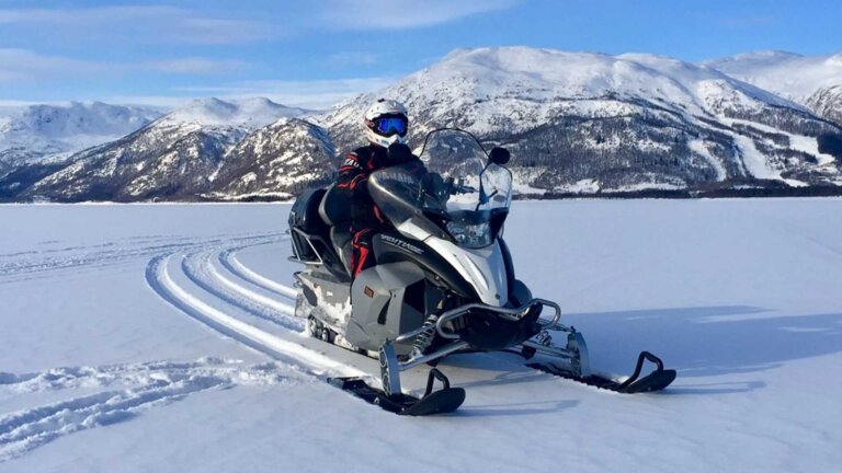 Snowmobile i snølandskap med fjell i bakgrunnen, perfekt for vintereventyr i Norge.