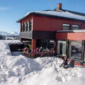 Koselig restaurant i fjellene, omringet av snø, med gjester som nyter solen og utsikten. Perfekt for après-ski.