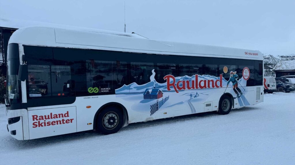 Buss fra Rauland Skisenter parkert i snøen, med illustrasjoner av skiaktiviteter på siden av bussen.