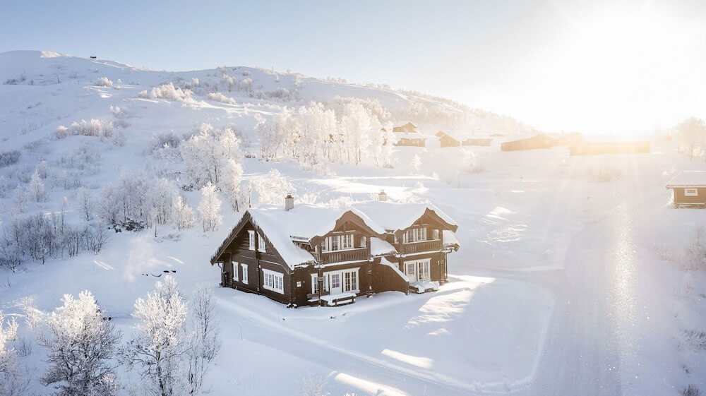 Tradisjonell norsk hytte i snødekt landskap med solskinn over fjellene i bakgrunnen.